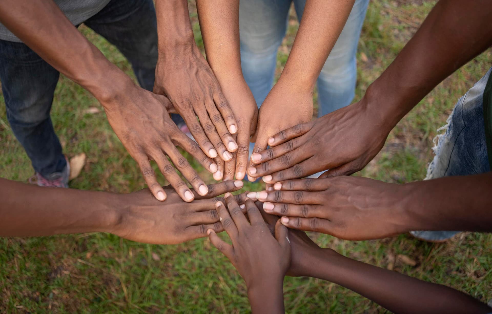 Young people of African descent joining hands in a circle on grass